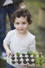 Портрет хлопчика, який тримає яєчну коробку і рослини в саду — стокове фото