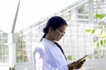Молодая женщина-ученый читает цифровой планшет в теплице лаборатории — стоковое фото