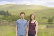 Adolescente casal de pé juntos no prado e olhando para longe sobre a paisagem rural — Fotografia de Stock