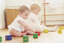 Baby sisters playing on floor with building blocks — Stock Photo
