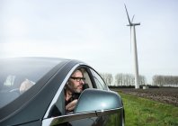 Hombre en coche con turbina eólica en segundo plano - foto de stock