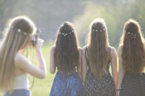 Visão traseira da menina adolescente fotografar amigos usando coberturas para a cabeça cadeia margarida no parque — Fotografia de Stock