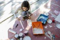 Chica en garaje revolviendo pintura en latas de pintura - foto de stock