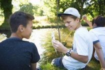 Boy holding fish with friends on river shore — Stock Photo