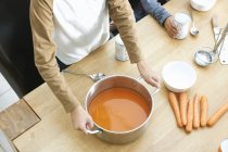 Cropped shot of boys at kitchen table holding pan of tomato soup — Stock Photo