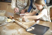 Foto recortada de mujer mayor y nietas cortando galletas de árbol de Navidad en el mostrador de la cocina - foto de stock