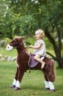 Porträt einer Kleinkindfrau, die Spielzeugpferd im Garten reitet — Stockfoto