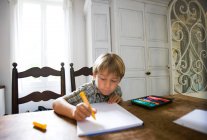 Мальчик с рисунком сидит за столом дома — стоковое фото