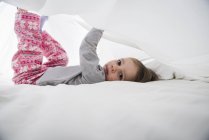 Portrait of female toddler lying between white bed sheets — Stock Photo