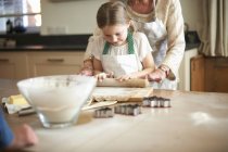 Senior woman and granddaughter rolling dough for Christmas tree cookies — Stock Photo