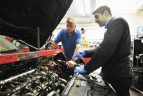 Male mechanics checking car engine in garage interior — Stock Photo