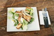 Teller mit Brot und Salat, Messer und Gabel auf Holztisch in Küche — Stockfoto