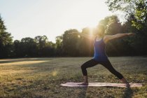 Зрелая женщина в парке, стоящая в позе йоги, вытянутые руки — стоковое фото