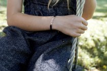 Mid section view of Girl on swing with bracelet on hand — Stock Photo