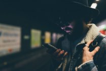 Молодий чоловік стоїть на платформі поїзда метро, дивлячись на смартфон — стокове фото