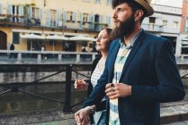 Couple with cocktails strolling along city canal — Stock Photo