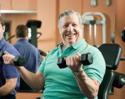 Homme plus âgé soulevant des poids dans la salle de gym — Photo de stock