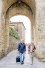 Tourist couple walking on cobbled street with wheeled suitcase in Siena, Tuscany, Italy — Stock Photo