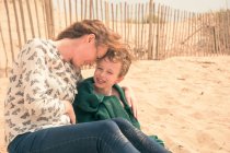 Jovem mulher sentada na praia com o filho envolto em cobertor — Fotografia de Stock