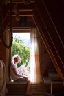 Retrato de adolescente sentada en el alféizar de la ventana del dormitorio iluminado por el sol - foto de stock