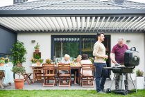 Deux hommes faisant un barbecue sur le patio au déjeuner en famille — Photo de stock