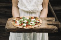 Cropped image of Woman holding homemade pizza on chopping board — Stock Photo