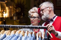 Quirky vintage pareja mirando ropa rail en antigüedades y vintage emporium - foto de stock