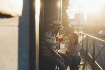 Casal sentado do lado de fora do café passeio iluminado pelo sol tendo coquetéis — Fotografia de Stock