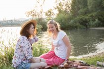 Two female friends relaxing beside lake — Stock Photo
