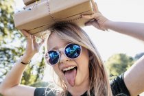 Дівчина стирчить язиком з коробкою на голові — стокове фото