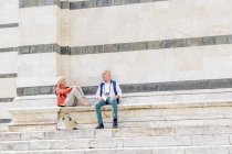 Pareja de turistas sentados en la escalera de la catedral de Siena, Toscana, Italia - foto de stock