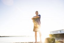 Low angle view of young man preparing for training on sunlit beach — Stock Photo