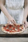 Обрезанный образ женщины кладет ингредиенты на домашнюю пиццу — стоковое фото