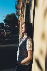 Junge Frau lehnt an sonnenbeschienene Wand — Stockfoto