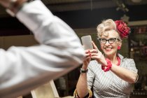 Quirky vintage woman photographing boyfriend in antiques emporium — Stock Photo