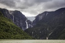 Cascada que fluye desde el glaciar al borde de la cara de roca montañosa, Parque Nacional Queulat, Chile - foto de stock