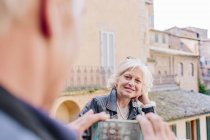 Vista sobre el hombro del turista masculino fotografiando esposa en la ciudad, Siena, Toscana, Italia - foto de stock