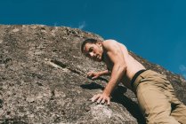 Bare chested young male climbing on boulder — Stock Photo