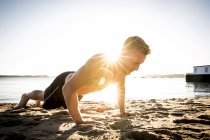 Giovane formazione e fare flessioni sulla spiaggia illuminata dal sole — Foto stock