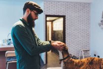 Uomo in cappello piatto cane da accarezzamento in appartamento — Foto stock