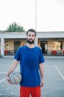 Портрет мужчины на баскетбольной площадке, держащего баскетбол, смотрящего в камеру — стоковое фото