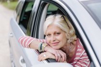 Portrait of mature woman looking out of car window on roadside — Stock Photo