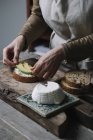 Donna che mette fette di avocado sul pane a fette con ricotta, sezione centrale — Foto stock