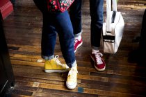 Jeans e scarpe da ginnastica indossati da coppia in piedi su pavimenti in legno — Foto stock