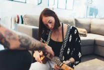 Jeune femme dans l'appartement apprendre à jouer ukulele de petit ami — Photo de stock