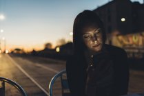 Молода жінка на вулиці дивиться на смартфон в сутінках — стокове фото