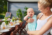 Junge Frau trägt kleine Tochter beim Familienessen am Terrassentisch — Stockfoto