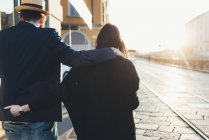 Vista posteriore di coppia passeggiando lungo il marciapiede illuminato dal sole — Foto stock