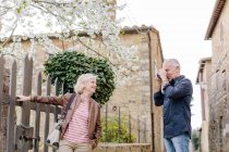 Senior male tourist photographing wife and blossom, Siena, Tuscany, Italy — Stock Photo