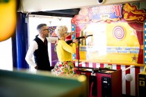 Pareja extraña disfrutando de galería de tiro en arcade de atracciones, Bournemouth, Inglaterra - foto de stock
